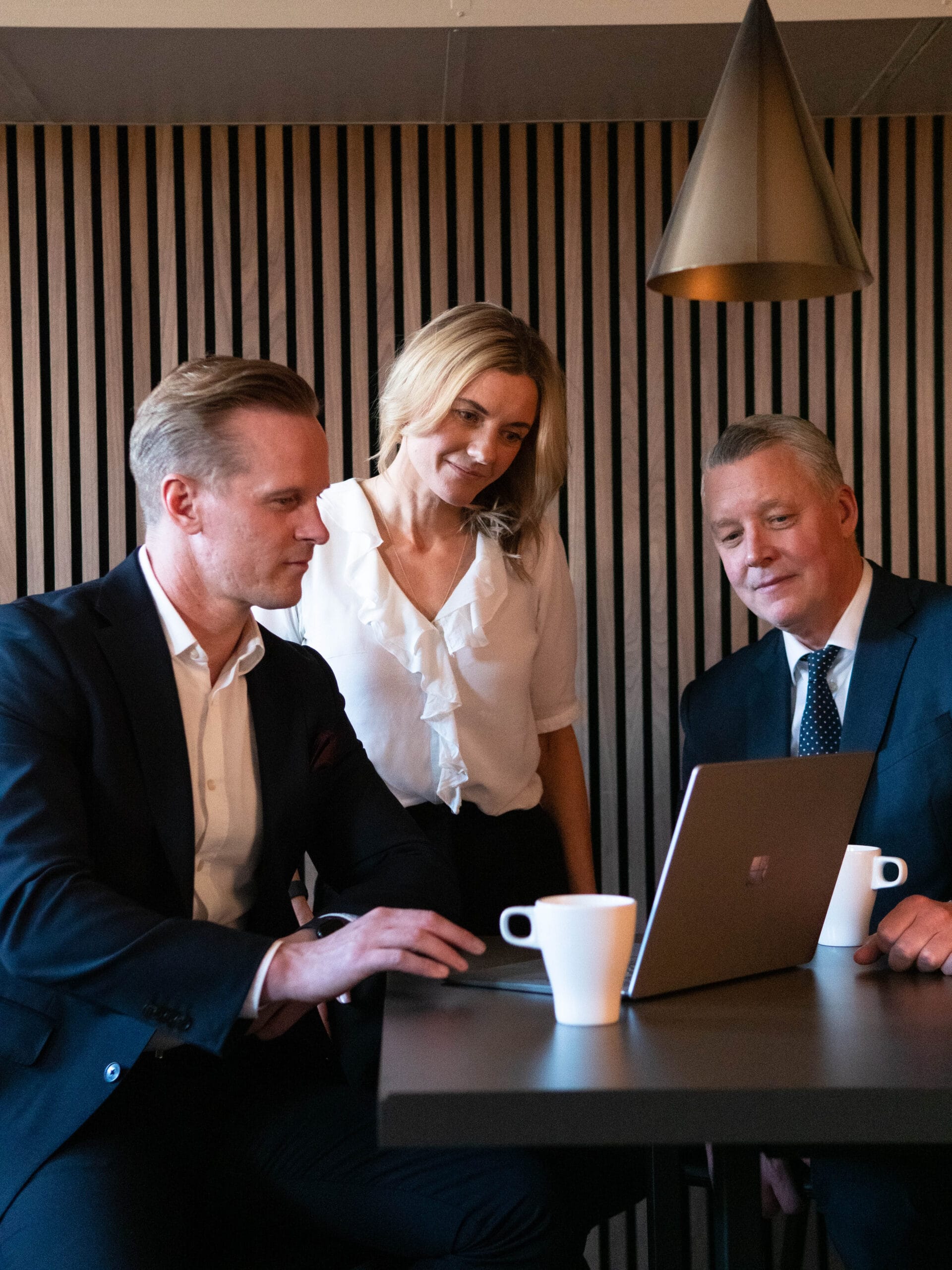 Tre kontorsklädda människor tittar på en dator