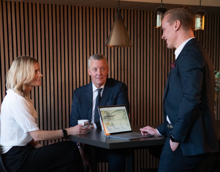 Tre välklädda personer i möte på modernt kontor.